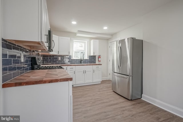 kitchen with stainless steel appliances, white cabinetry, light hardwood / wood-style flooring, wood counters, and decorative backsplash