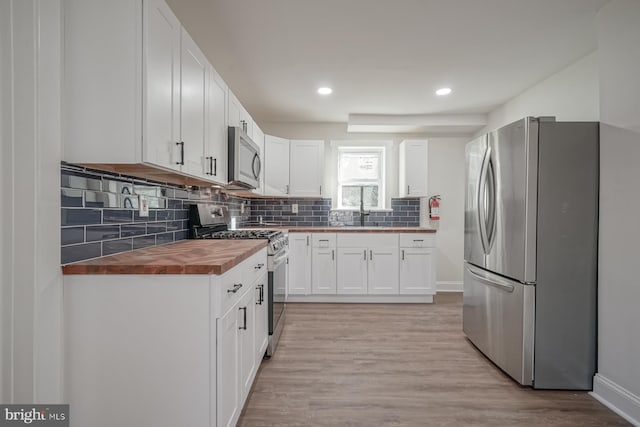 kitchen featuring white cabinetry, light hardwood / wood-style floors, wood counters, decorative backsplash, and appliances with stainless steel finishes