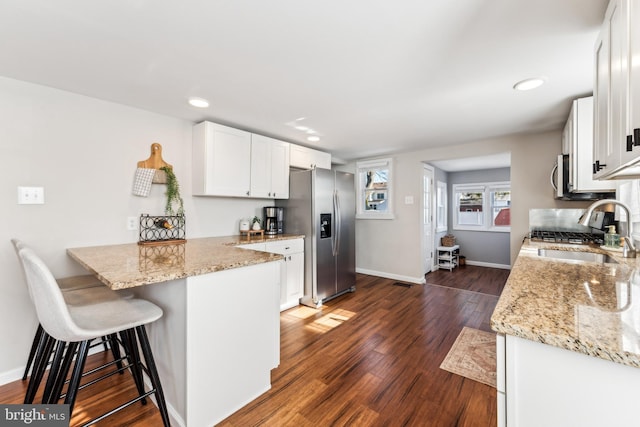 kitchen featuring sink, white cabinetry, stainless steel appliances, light stone counters, and kitchen peninsula