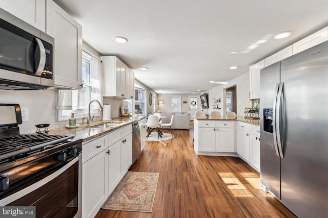 kitchen featuring sink, kitchen peninsula, stainless steel appliances, light stone countertops, and white cabinets