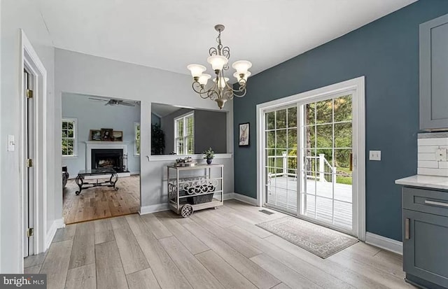 doorway to outside with ceiling fan with notable chandelier and light hardwood / wood-style floors