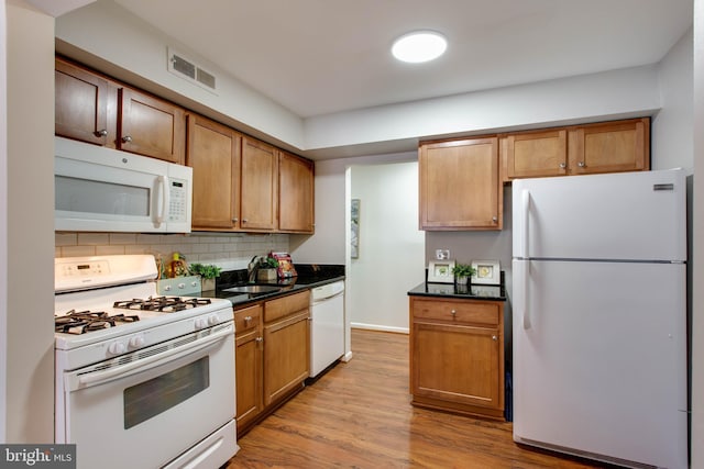 kitchen featuring white appliances, tasteful backsplash, light wood-type flooring, sink, and dark stone counters