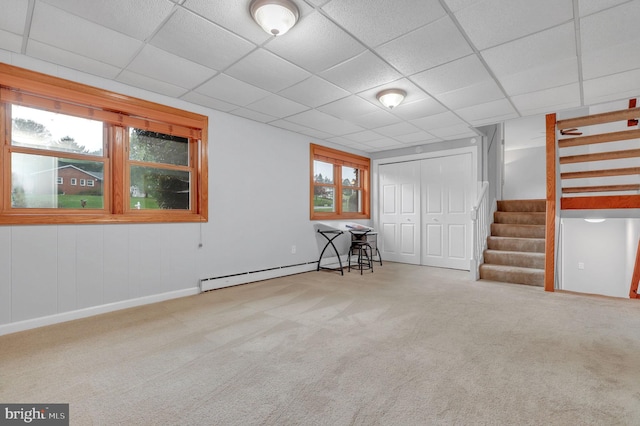 basement with carpet, a baseboard heating unit, a drop ceiling, and a healthy amount of sunlight