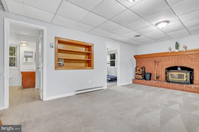 unfurnished living room featuring a wood stove, baseboard heating, built in features, and a paneled ceiling