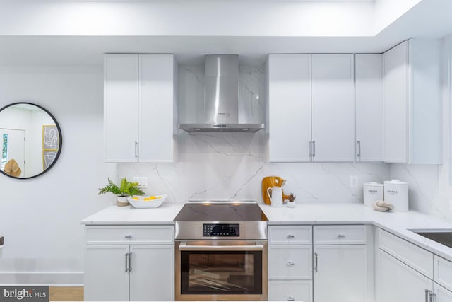 kitchen with decorative backsplash, white cabinetry, electric range, and wall chimney exhaust hood