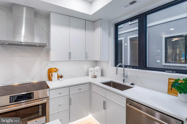 kitchen with light stone countertops, wall chimney exhaust hood, white cabinets, appliances with stainless steel finishes, and sink