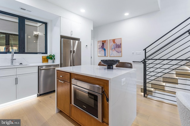 kitchen featuring sink, white cabinetry, light hardwood / wood-style floors, a kitchen island, and appliances with stainless steel finishes