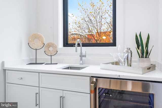 bar featuring light stone counters, white cabinets, beverage cooler, and sink