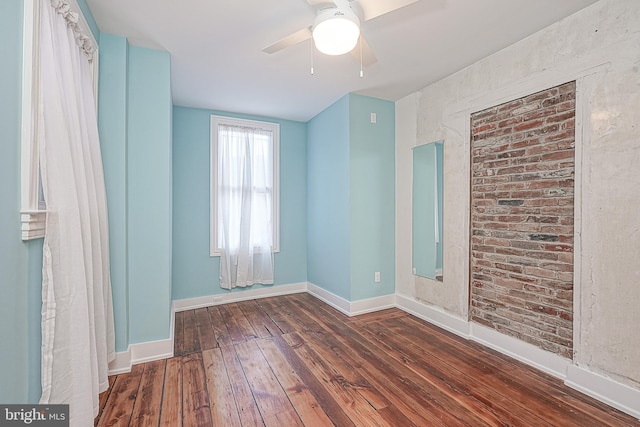 unfurnished room featuring ceiling fan, dark wood-type flooring, and brick wall