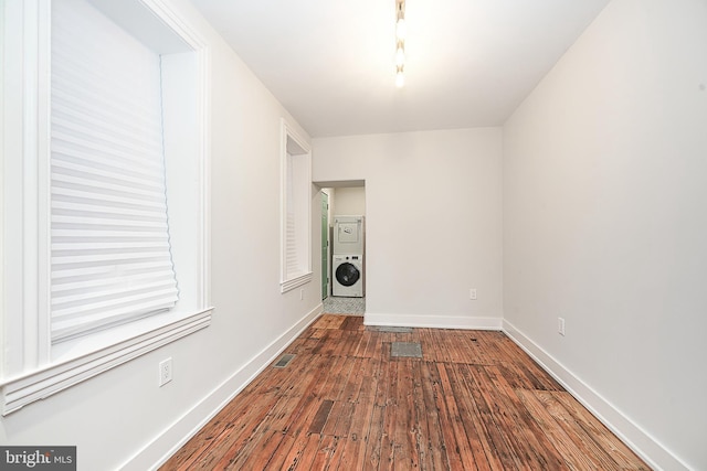 unfurnished room featuring stacked washer / drying machine and wood-type flooring