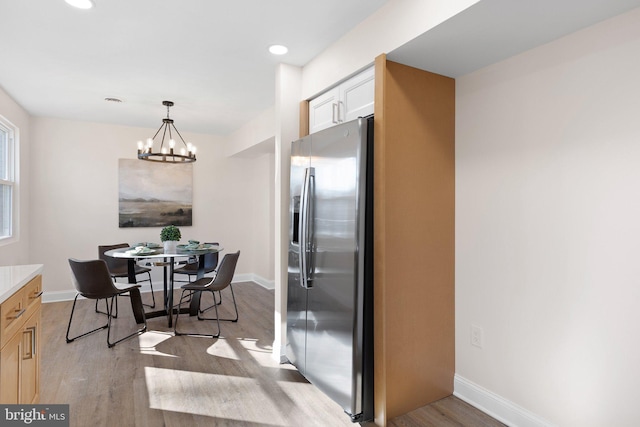 kitchen with light hardwood / wood-style flooring, decorative light fixtures, stainless steel refrigerator with ice dispenser, an inviting chandelier, and white cabinets