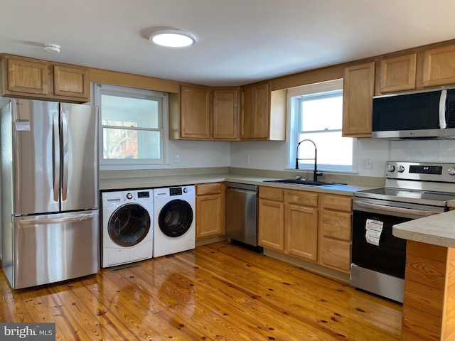 kitchen featuring appliances with stainless steel finishes, sink, washing machine and clothes dryer, and light hardwood / wood-style flooring