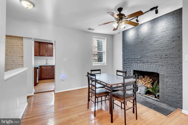 dining area with baseboards, visible vents, light wood finished floors, a ceiling fan, and a fireplace