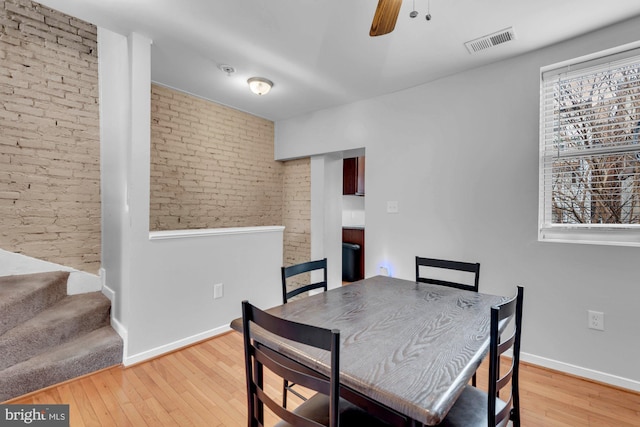 dining space featuring visible vents, brick wall, a ceiling fan, baseboards, and light wood-style floors