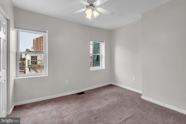 carpeted spare room with baseboards, visible vents, and ceiling fan