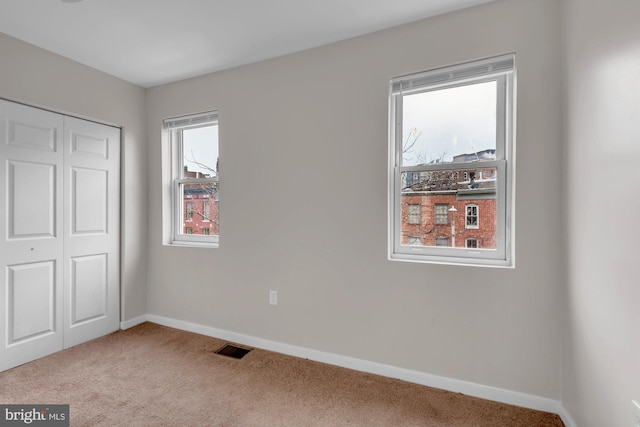 unfurnished bedroom with light colored carpet, visible vents, a closet, and baseboards