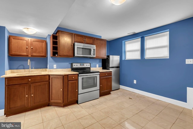 kitchen with light countertops, stainless steel appliances, a sink, brown cabinets, and open shelves