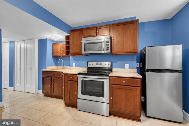 kitchen with a sink, light countertops, appliances with stainless steel finishes, brown cabinetry, and open shelves