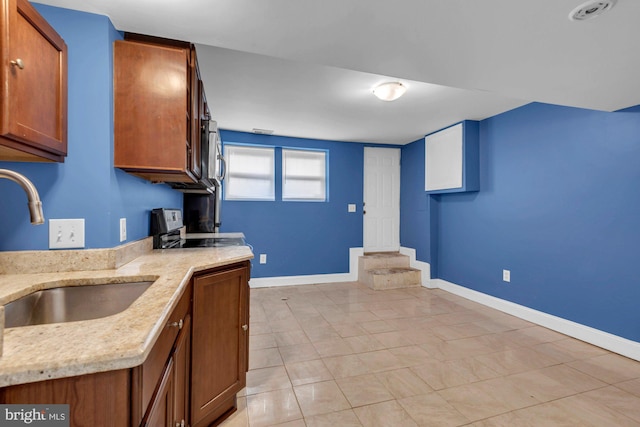 kitchen with baseboards, range with electric cooktop, a sink, light stone countertops, and brown cabinetry