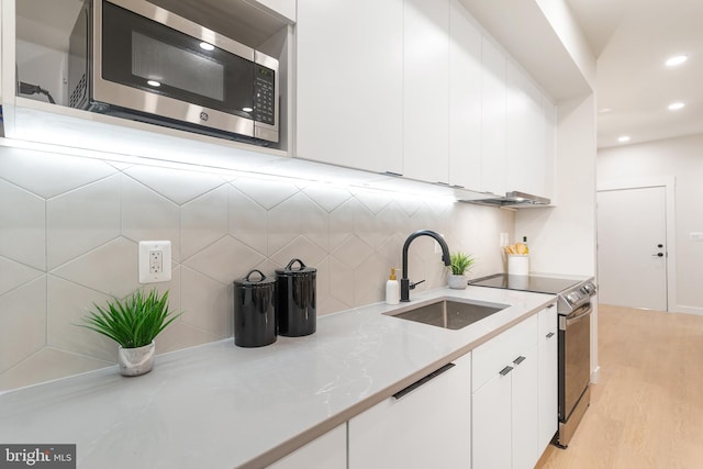 kitchen with appliances with stainless steel finishes, light hardwood / wood-style floors, white cabinets, and sink