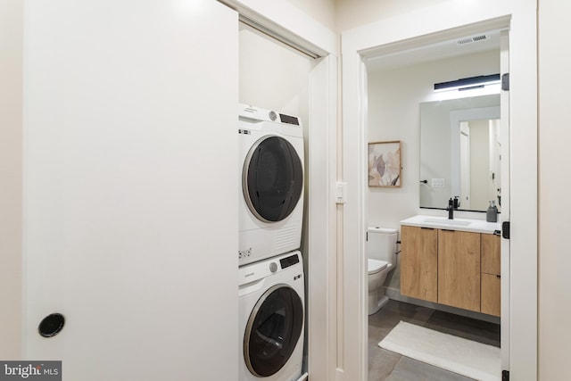 clothes washing area featuring stacked washing maching and dryer, light tile patterned flooring, and sink