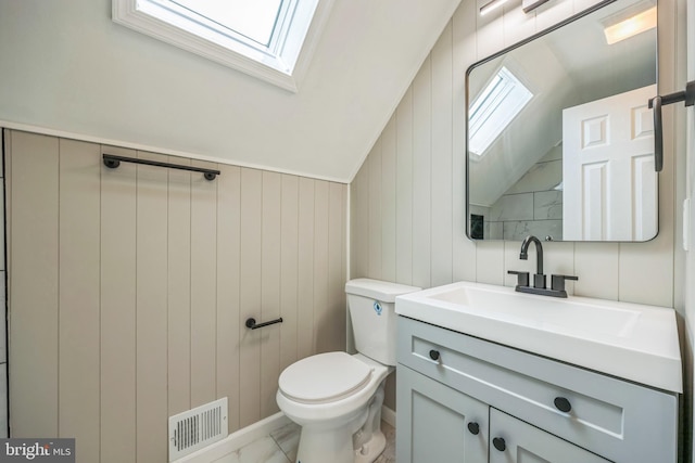 bathroom with lofted ceiling with skylight, wood walls, and toilet