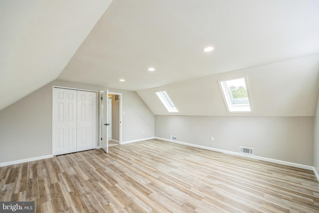 bonus room with lofted ceiling with skylight and light wood-type flooring