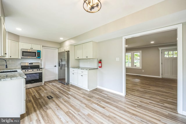 kitchen with appliances with stainless steel finishes, light hardwood / wood-style floors, decorative backsplash, sink, and white cabinetry