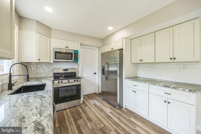 kitchen featuring appliances with stainless steel finishes, light stone countertops, decorative backsplash, white cabinets, and sink