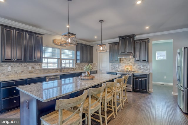 kitchen with stainless steel appliances, pendant lighting, a kitchen bar, a kitchen island, and sink