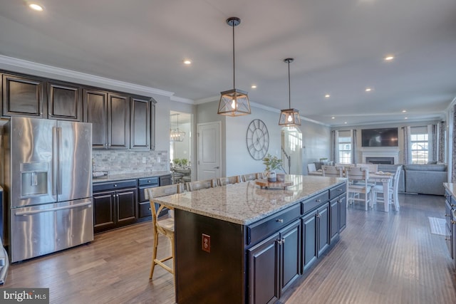 kitchen featuring decorative light fixtures, a center island, stainless steel fridge with ice dispenser, and dark brown cabinetry