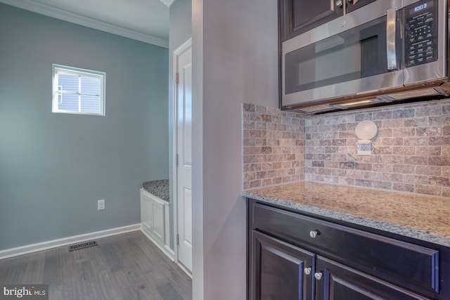 kitchen featuring crown molding, light stone counters, and dark brown cabinetry