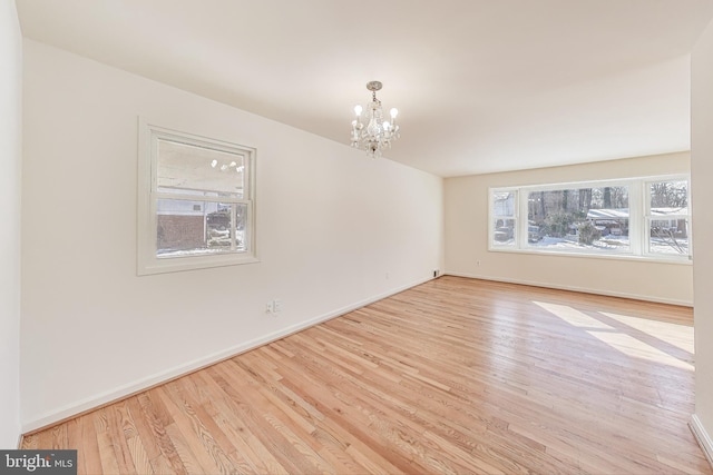 spare room with an inviting chandelier and light hardwood / wood-style floors