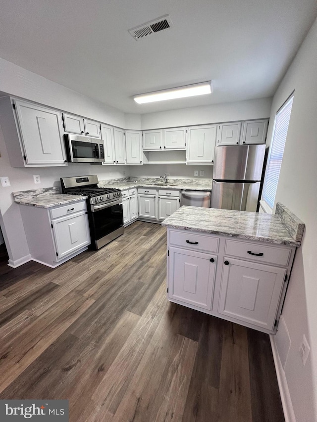 kitchen featuring appliances with stainless steel finishes, light stone counters, dark hardwood / wood-style floors, sink, and white cabinetry