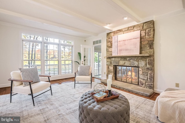 living area with hardwood / wood-style floors, beam ceiling, and a stone fireplace