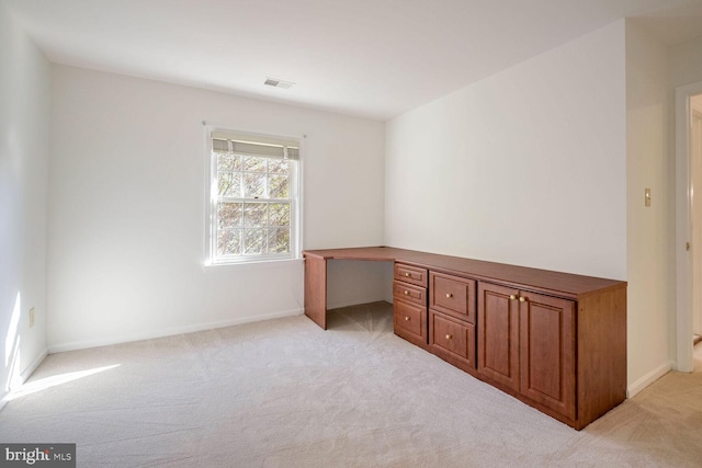 unfurnished office featuring built in desk and light colored carpet