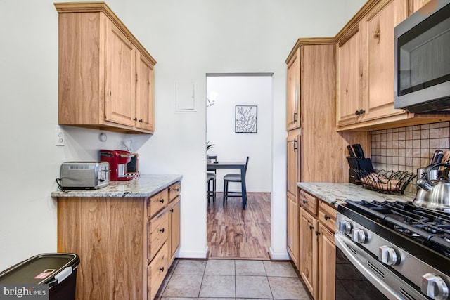 kitchen featuring light stone counters, light tile patterned floors, stainless steel appliances, and tasteful backsplash