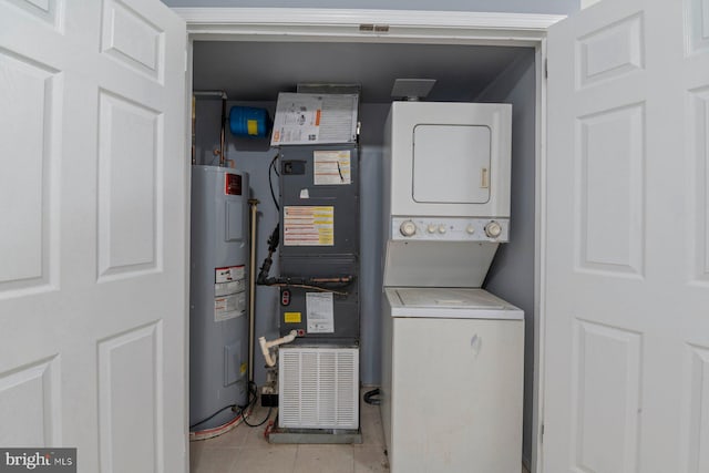 laundry area featuring stacked washer and dryer, light tile patterned floors, water heater, and heating unit