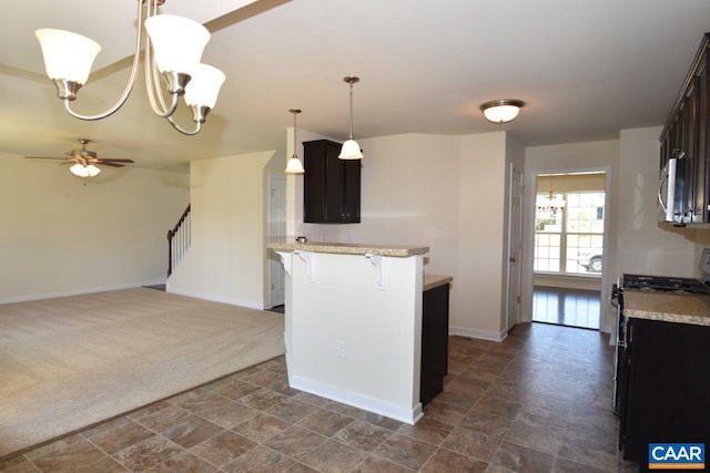 kitchen featuring dark carpet, appliances with stainless steel finishes, a breakfast bar, pendant lighting, and ceiling fan with notable chandelier