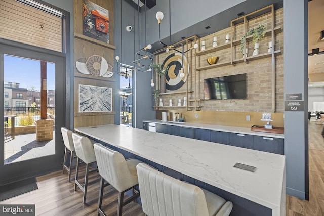 kitchen with light stone counters, light hardwood / wood-style flooring, hanging light fixtures, a breakfast bar area, and sink