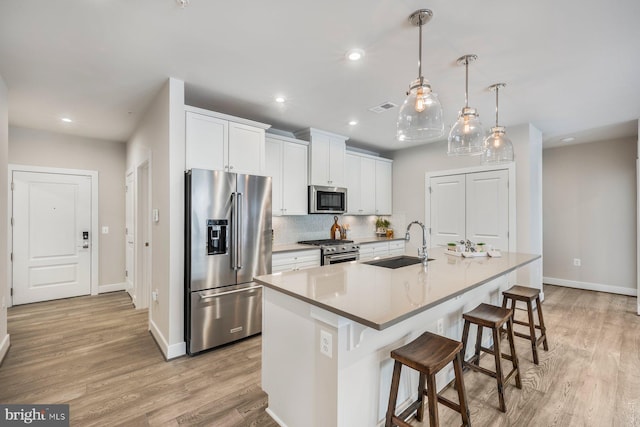 kitchen with sink, white cabinetry, an island with sink, backsplash, and premium appliances