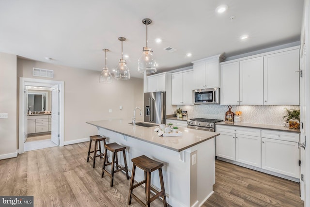 kitchen with sink, white cabinetry, high end appliances, hanging light fixtures, and a kitchen island with sink