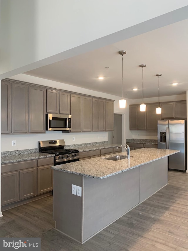 kitchen with appliances with stainless steel finishes, decorative light fixtures, sink, light stone counters, and a center island with sink