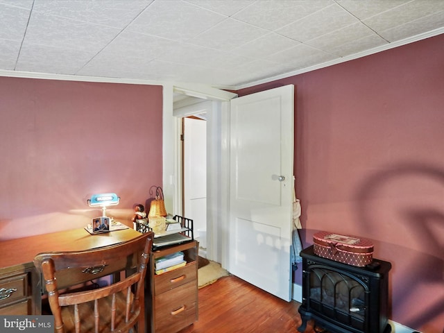 home office with hardwood / wood-style flooring, crown molding, and a wood stove