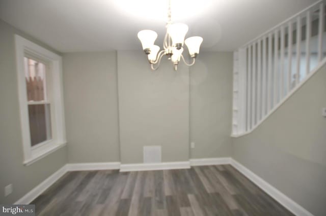 unfurnished dining area with dark wood-type flooring and an inviting chandelier