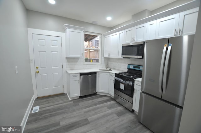 kitchen with hardwood / wood-style flooring, stainless steel appliances, decorative backsplash, white cabinets, and sink