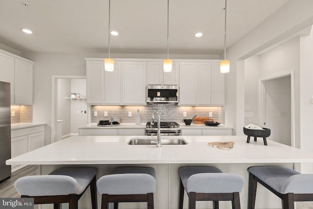 kitchen with stainless steel appliances, white cabinets, an island with sink, decorative backsplash, and pendant lighting