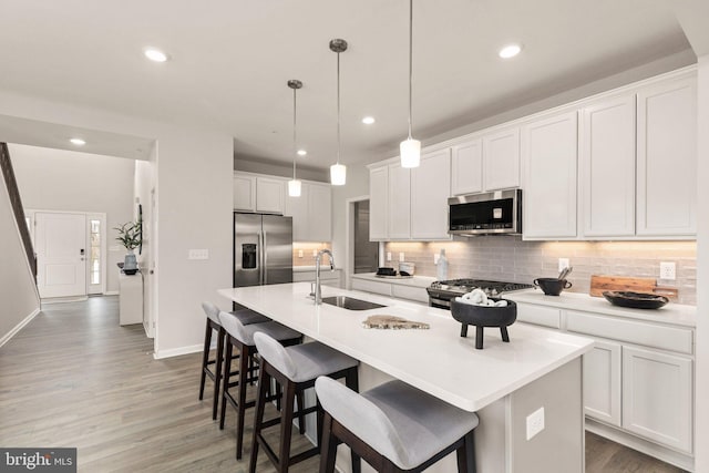 kitchen featuring hanging light fixtures, an island with sink, white cabinetry, appliances with stainless steel finishes, and sink