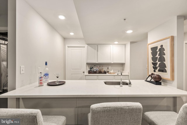 kitchen with sink, kitchen peninsula, a kitchen bar, and white cabinetry