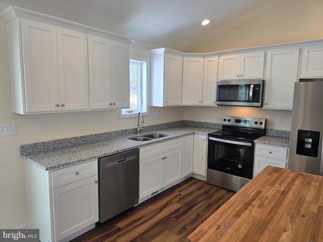 kitchen featuring vaulted ceiling, sink, light stone countertops, appliances with stainless steel finishes, and white cabinets